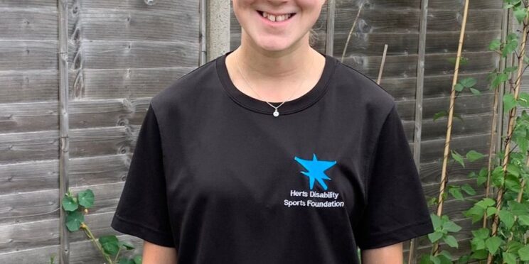 Photo of Abi in her HDSF t-shirt. She is standing in a garden surrounded by flowers