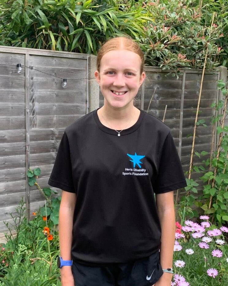 Photo of Abi in her HDSF t-shirt. She is standing in a garden surrounded by flowers